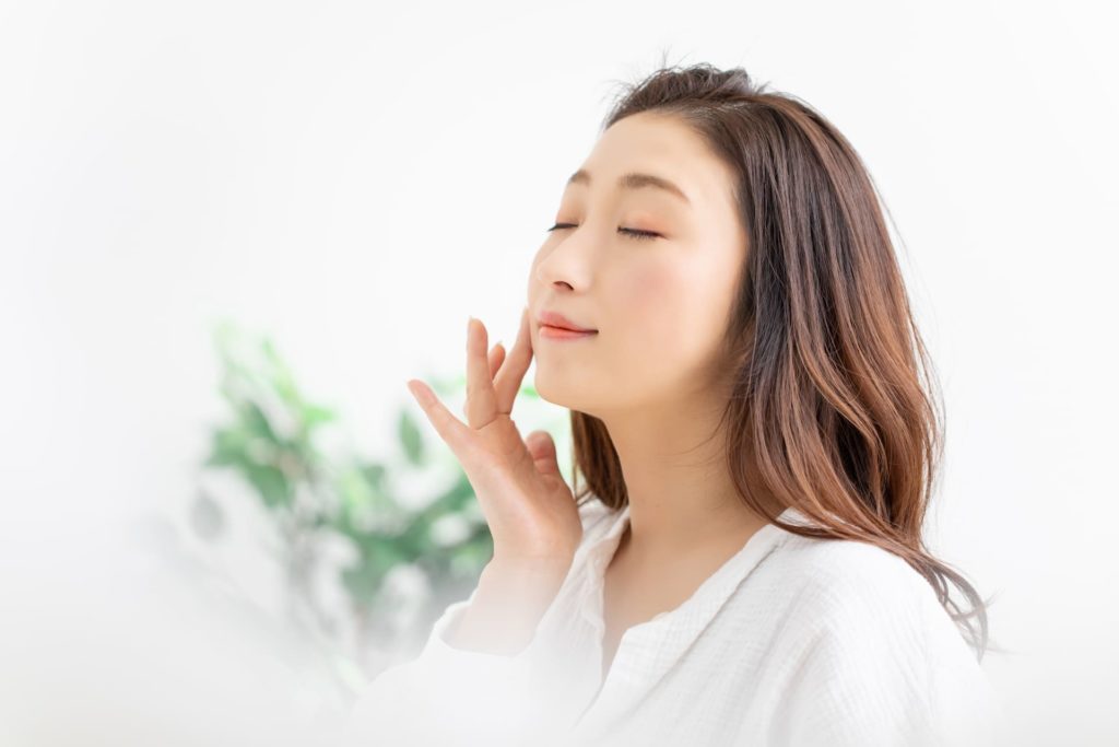 目を閉じて頬を触っている女性