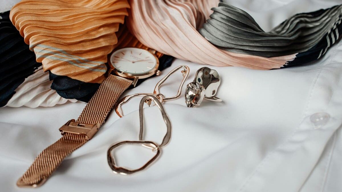 Accessories including silk scarves, a wristwatch, glasses, and rings placed on a white shirt.