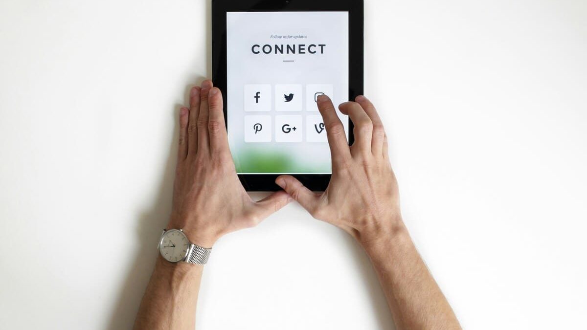 Hands holding a tablet with social media icons (Facebook, Twitter, Pinterest, Google+, Vine) on the screen. The screen displays the word 'CONNECT