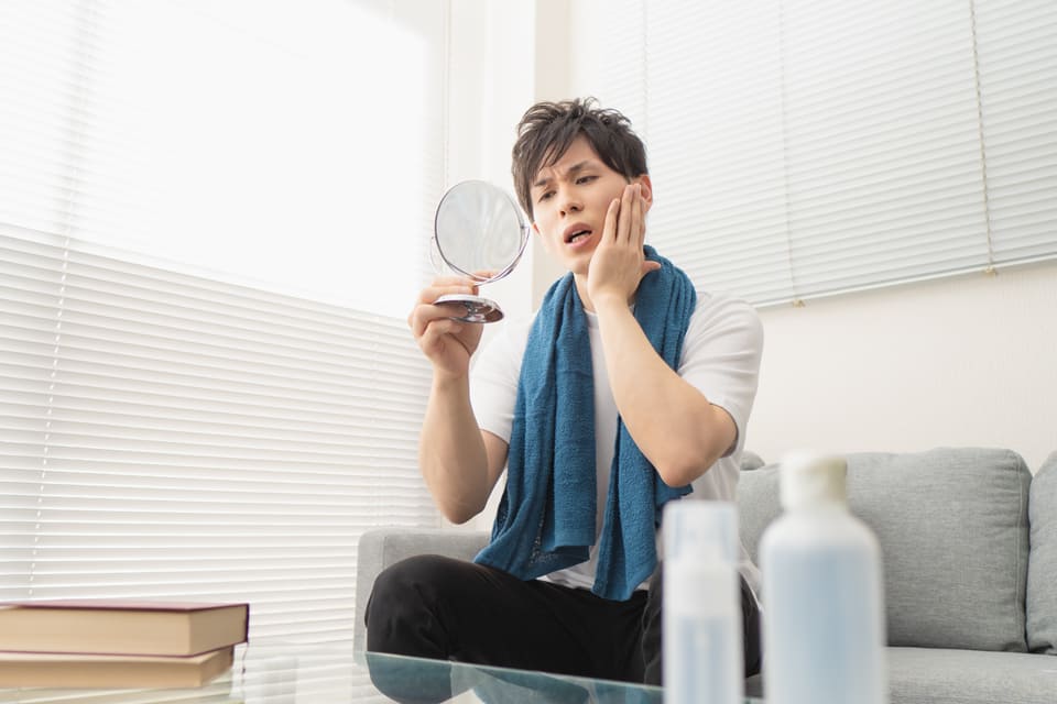 鏡を見ながら顔を気にする男性。