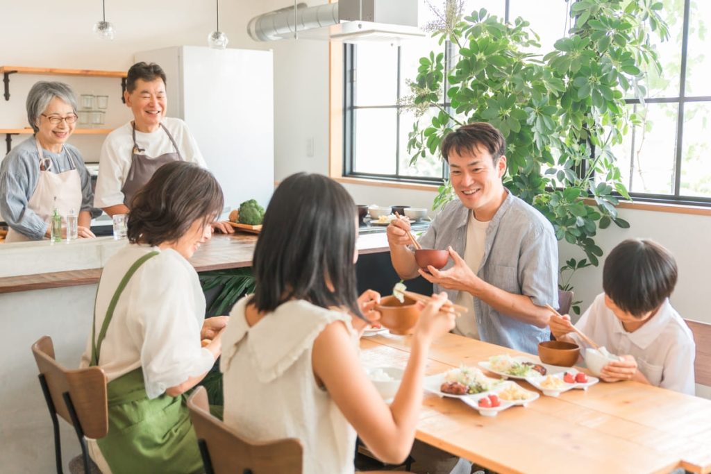 家族がダイニングテーブルで楽しく食事をしている様子。背景にはキッチンがあり、祖父母が微笑みながら見守っている。