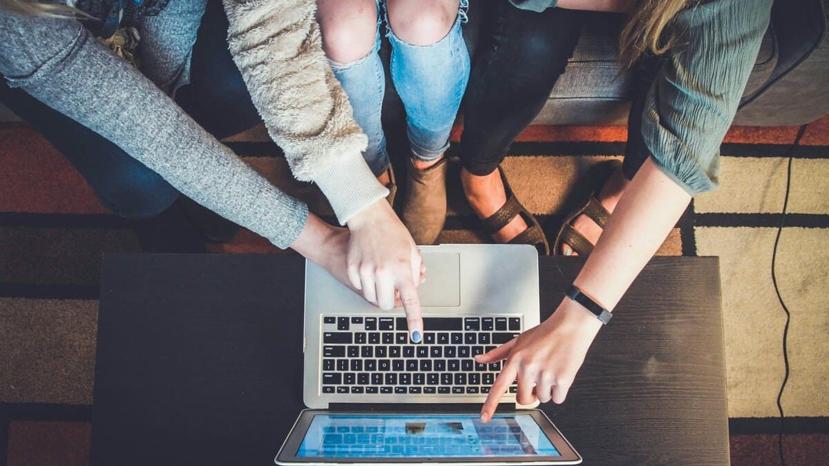 Three people pointing at a laptop screen, discussing something while sitting together on a couch