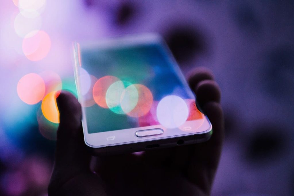 カラフルなぼやけたボケ効果のライトを背景に、スマートフォンを手に持つ人物