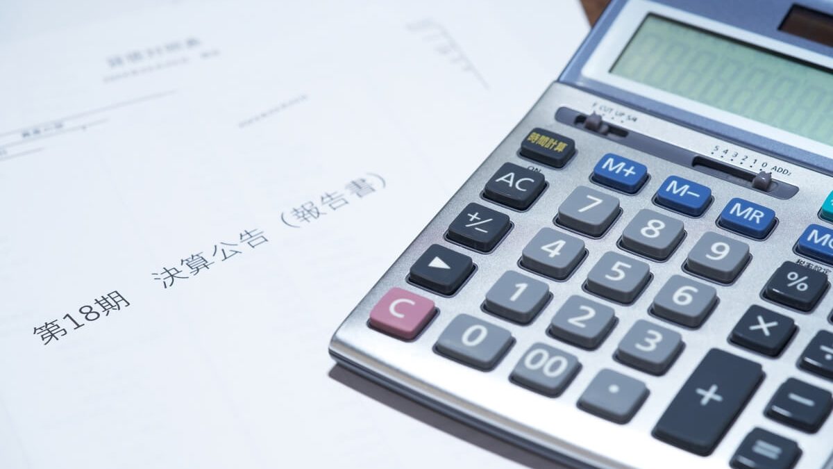 A calculator placed on financial documents written in Japanese, including the phrase "第18期 決算公告（報告書）" (18th fiscal term financial report)