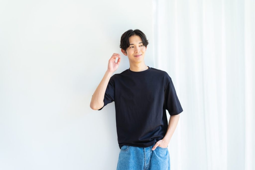 爽やかな男性が白い壁の前で立って微笑んでいる