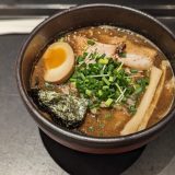 A bowl of miso ramen topped with a soft-boiled egg, chashu pork slices, green onions, bamboo shoots, seaweed, and sesame seeds, served in a dark bowl on a black tray.