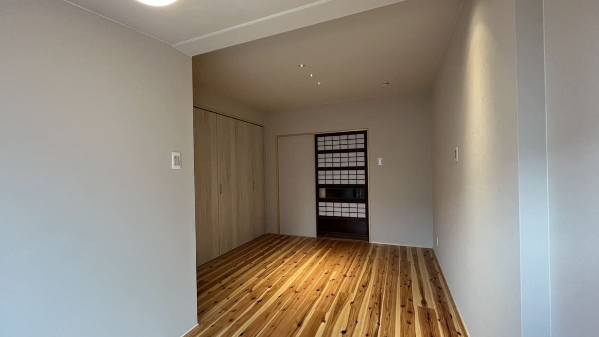 A simple room with light wood flooring, sliding wooden closet doors, and a traditional Japanese sliding door (shoji) at the back. The space is minimalistic with soft lighting.