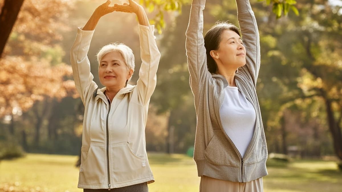 Two middle-aged women stretching in a park. They are raising their arms and stretching with relaxed expressions as the morning sunlight filters through the autumn trees, creating a calm and peaceful atmosphere.