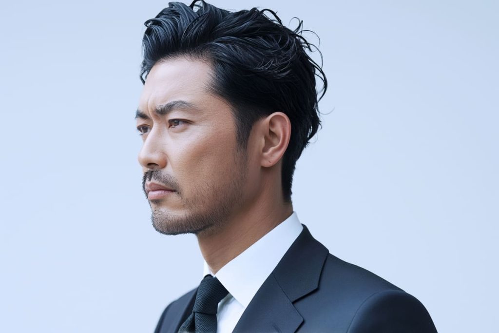 黒いスーツとネクタイを着た男性が、真剣で決意に満ちた表情で遠くを見つめている。オールバックの髪型と整えられたひげが自信を感じさせる。