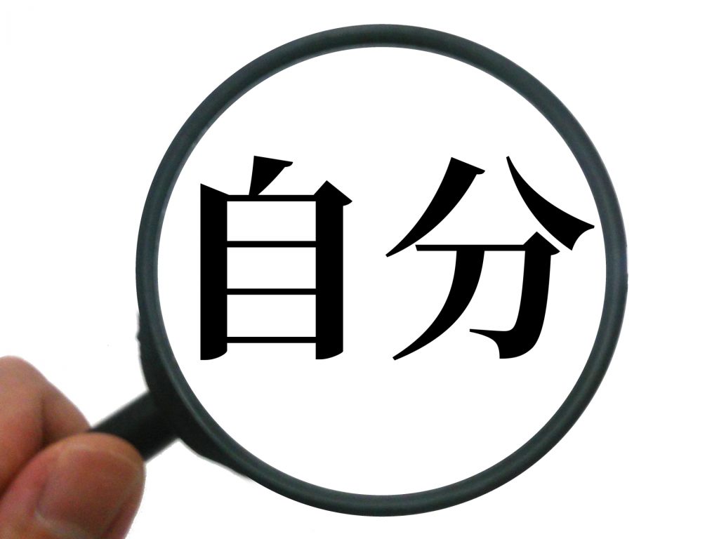 手に持った虫眼鏡で「自分」という漢字を拡大しているイメージ。