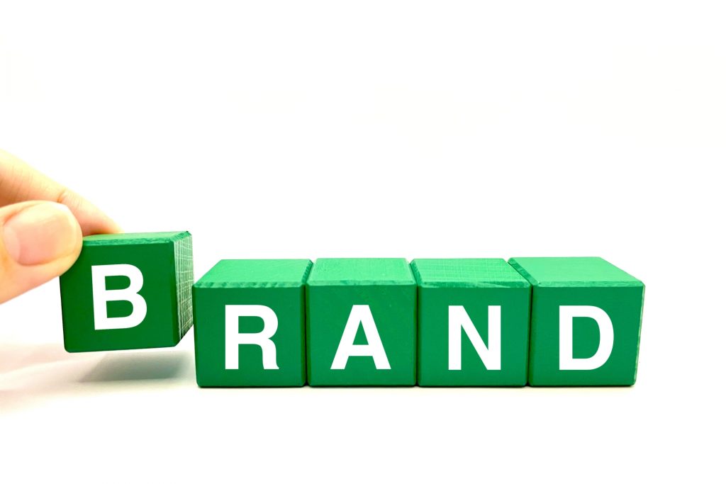緑色の積み木で作られた「BRAND」という文字。左端の積み木に手が添えられており、ブランドコンセプトや企業イメージを表現するイメージ。