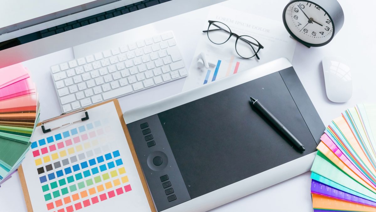 A designer’s workspace with a color chart, pen tablet, computer, and keyboard.