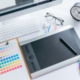 A designer’s workspace with a color chart, pen tablet, computer, and keyboard.
