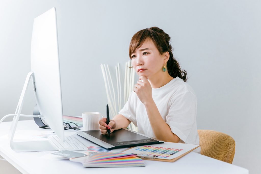 グラフィックタブレットを使い、真剣な表情で作業する女性デザイナーの画像。