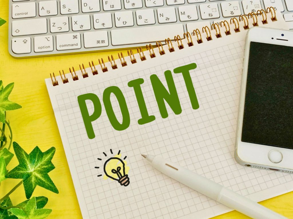 ノートに「POINT」と書かれたメモ、スマートフォンとキーボードが並ぶデスク上の様子。
