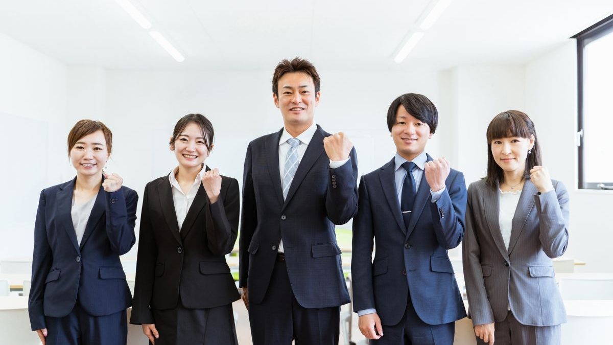Five business people in suits making a victory pose