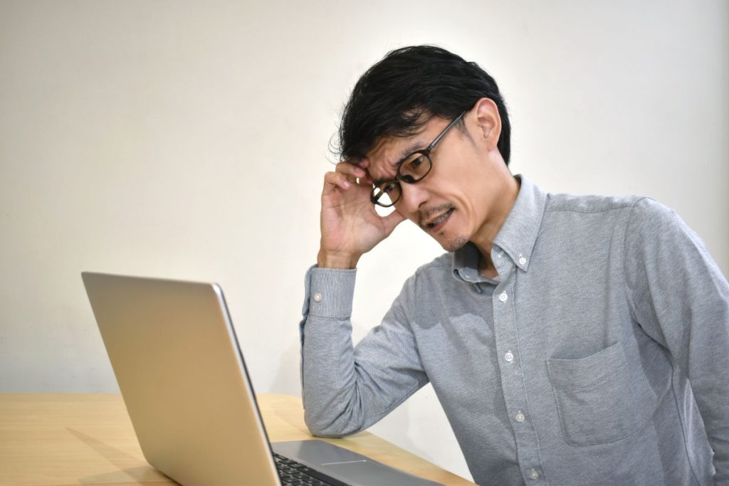ノートパソコンに向かって心配そうな表情を浮かべる男性の画像。