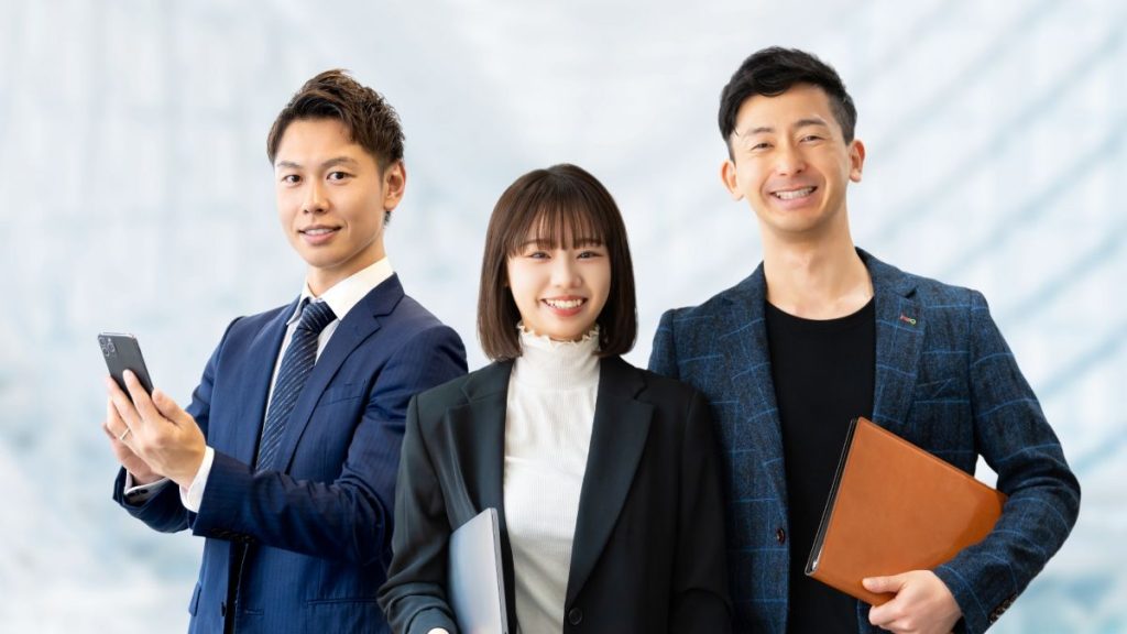 スーツ姿のビジネスパーソン3人が並んで笑顔を見せている