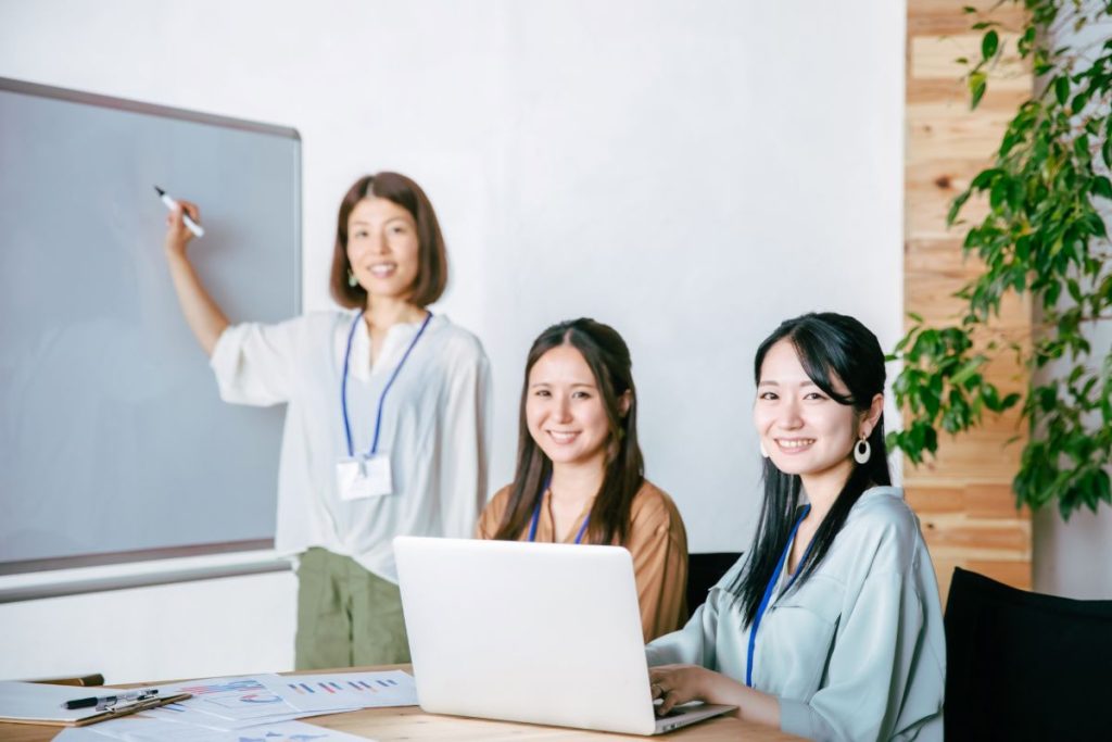 ホワイトボードの前で研修を受ける二人の女性社員とコーチの女性の画像。