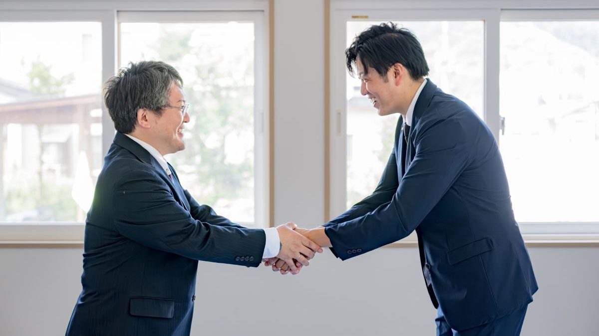 An image of a senior executive and a young male employee firmly shaking hands.
