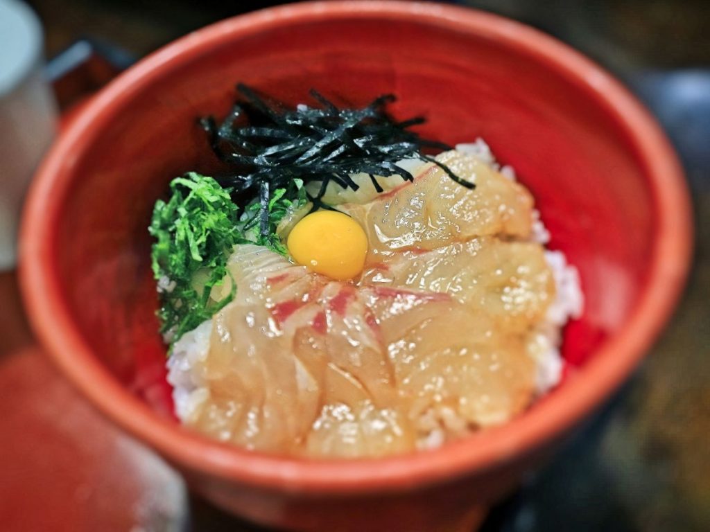 鯛の刺身、卵黄、刻み海苔、大葉がご飯にのった鯛めしの写真
