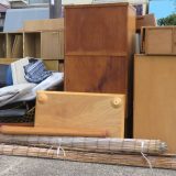 Bulky unwanted items such as furniture, futons, carpets, and shelves are piled up outdoors. The image represents the idea of moving out, major cleaning, or bulky waste disposal.