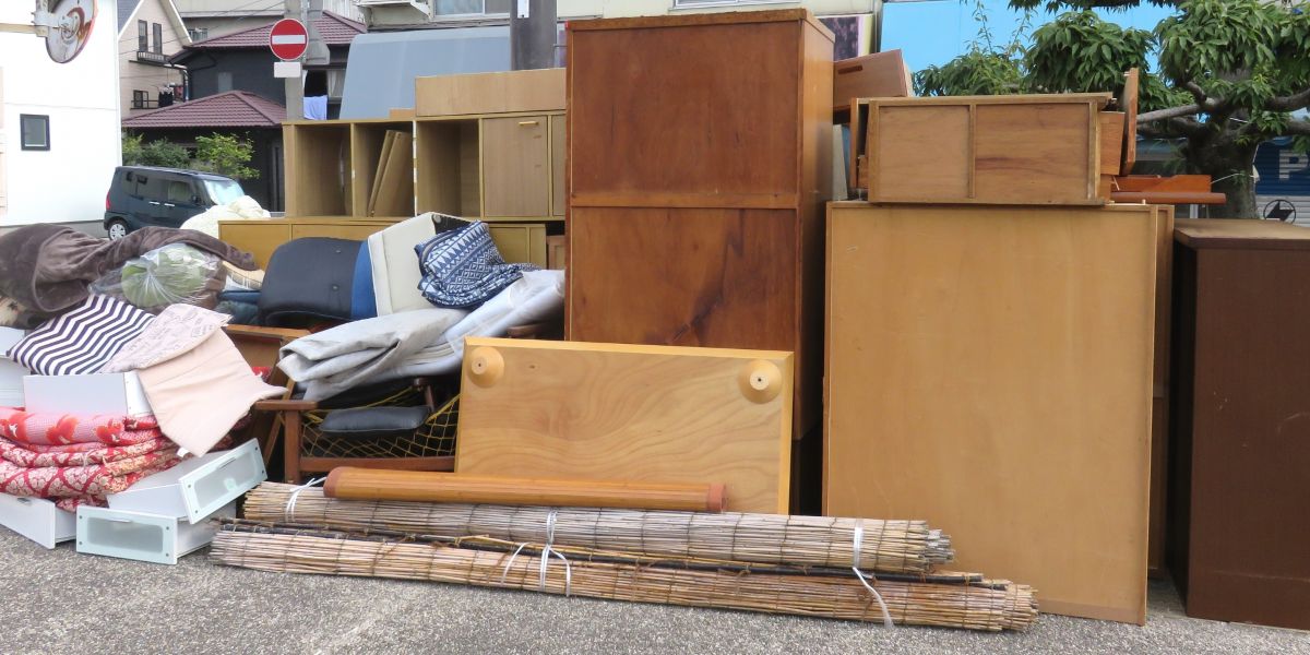 Bulky unwanted items such as furniture, futons, carpets, and shelves are piled up outdoors. The image represents the idea of moving out, major cleaning, or bulky waste disposal.
