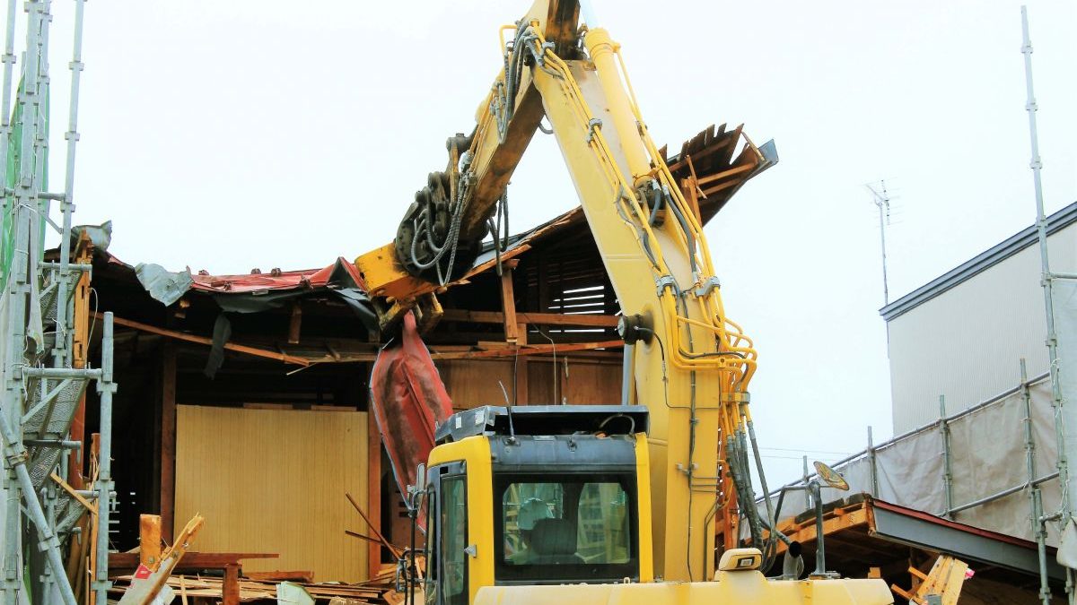 Image of a yellow excavator demolishing a wooden house.