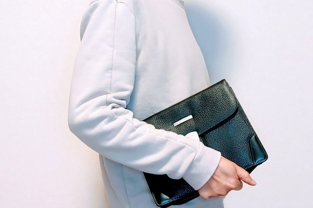 シンプルな服装の人物が黒いレザークラッチバッグを抱えている様子。洗練された大人のスタイルを演出。