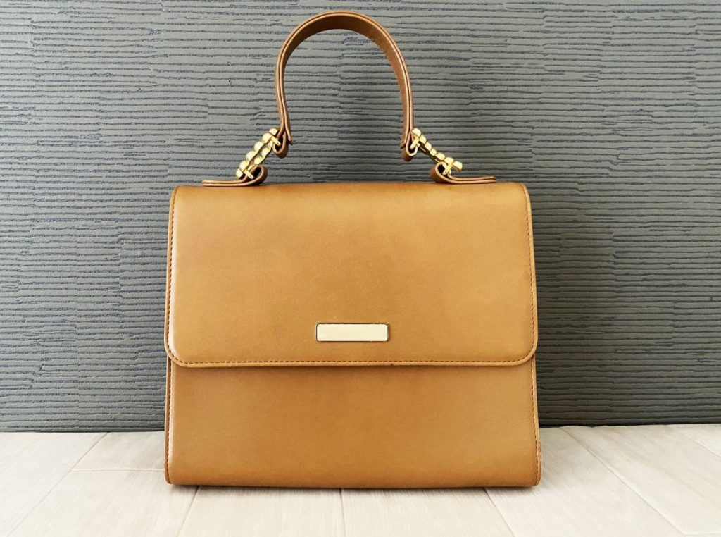 シンプルで上品なキャメル色のレザーハンドバッグが床の上に置かれている画像。