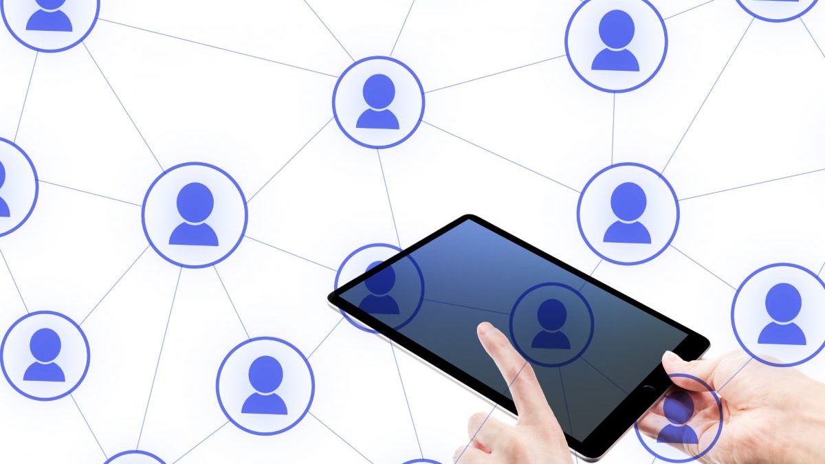 A hand operating a tablet device in front of a digital illustration showing blue user icons connected in a network. The image represents the expansion of digital connections, social networking, and online communities.