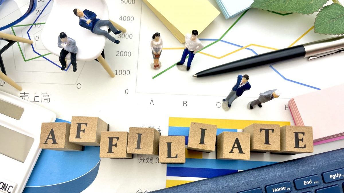 An image showing a wooden block labeled “Affiliate” placed on a desk, surrounded by sales data charts and a laptop keyboard. It evokes the concept of affiliate income and web marketing analysis.