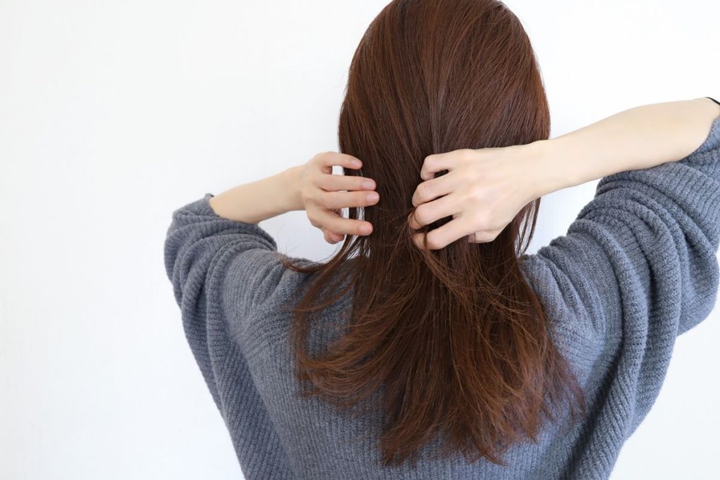 ニットを着た後ろ姿の女性が髪を束ねるように触っている様子。ニット素材との摩擦が起きやすい冬のヘアケア場面。