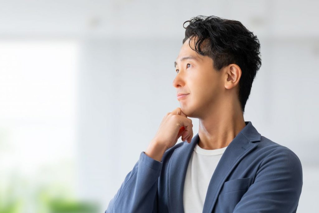 スーツを着た若い男性が顎に手を当てて考え事をしている様子。

