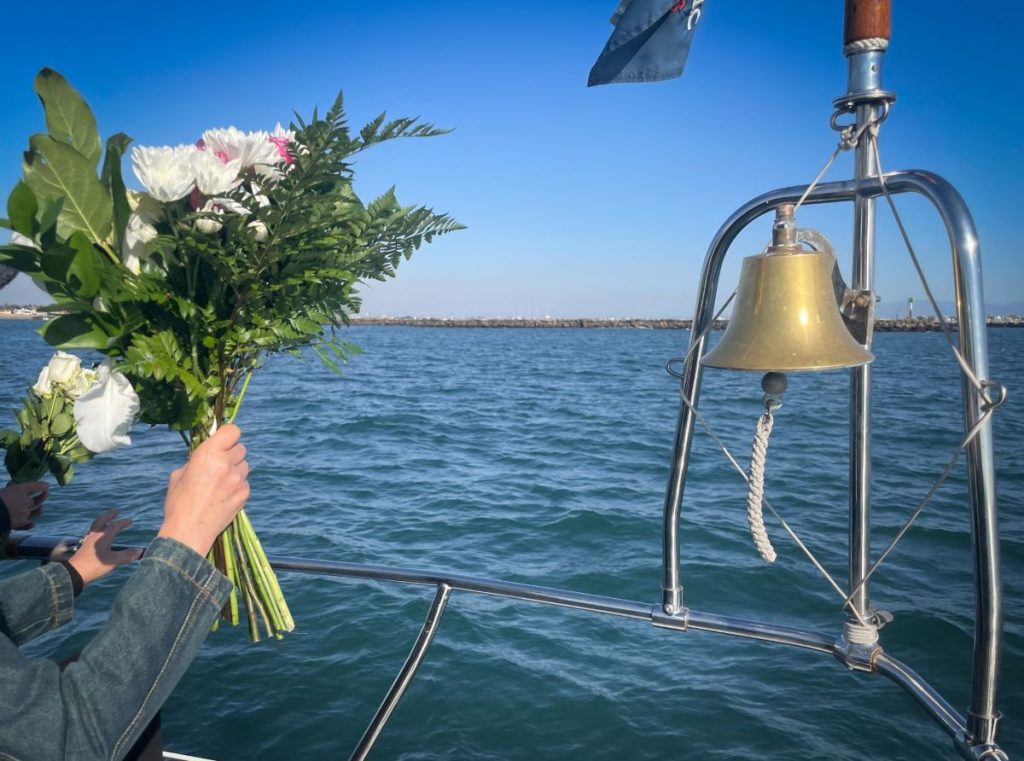 海の上で白い花束を手に持ち、海洋散骨を行う様子。青空と波が故人との別れを静かに彩る。