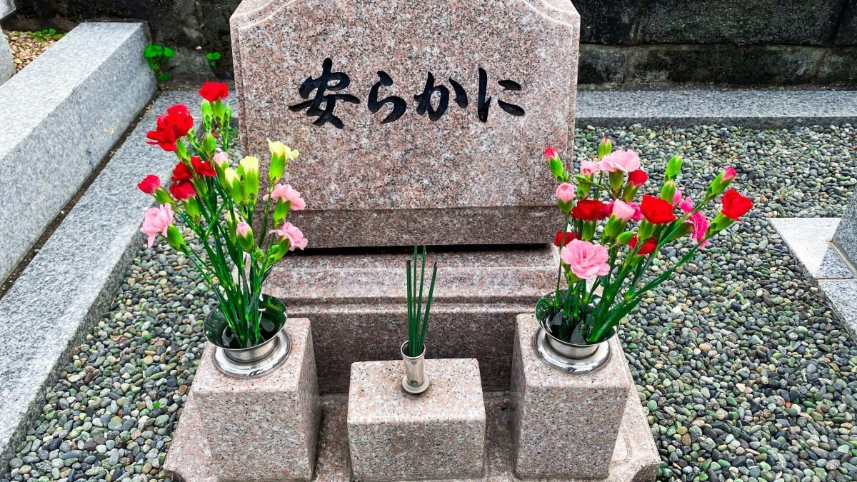 A pet grave made of pink granite with the words "Rest in Peace" engraved. Carnations are placed on both sides, creating a serene atmosphere.