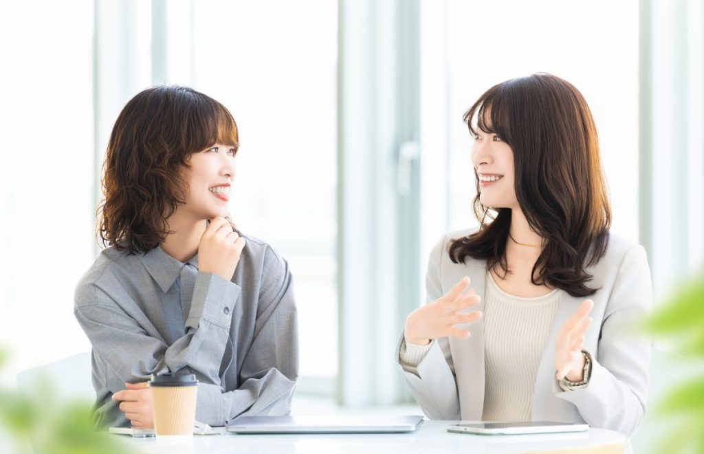 明るいオフィスで向かい合った2人の女性が楽しそうに会話をしている様子。