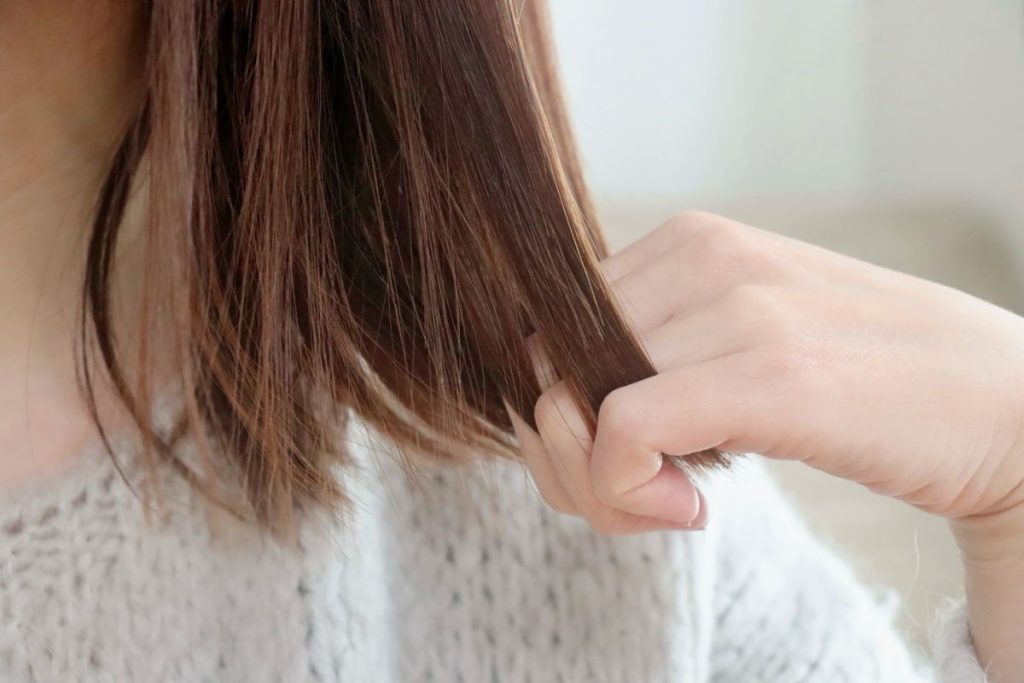 女性が髪の毛をすいている手元の画像、毛先のダメージを気にしているイメージ。