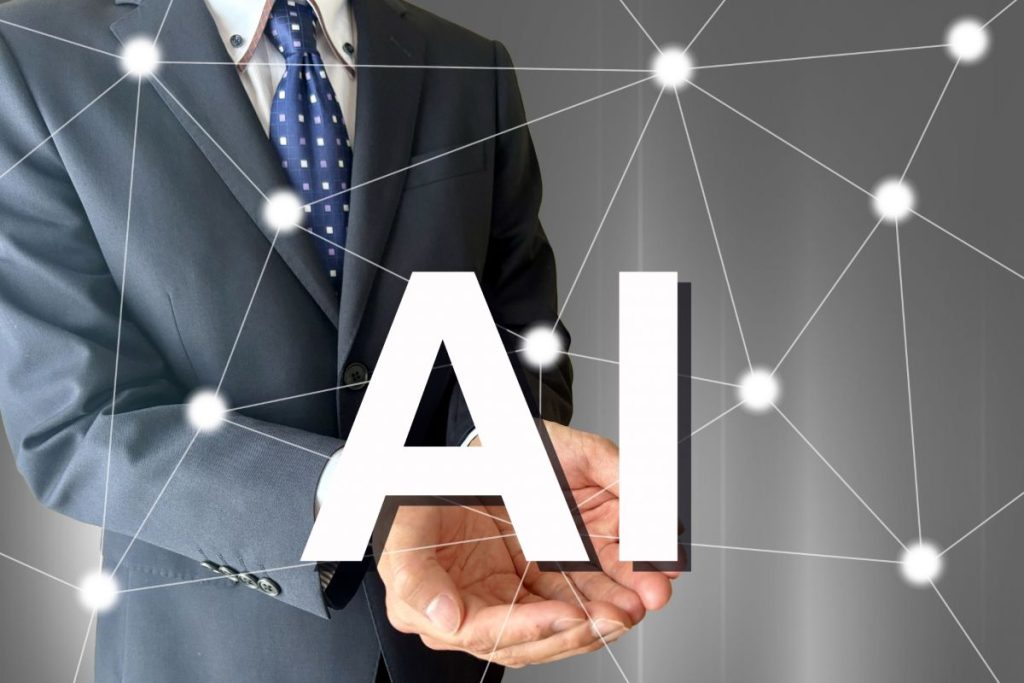 ビジネスマンが手のひらの上に「AI」の文字を浮かべ、背景にはデジタルネットワークが広がっている画像。AI技術とビジネスの融合を象徴。