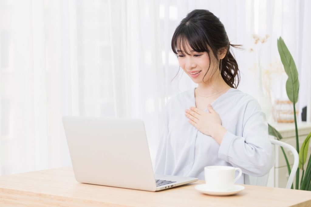 パソコン画面の前で、女性が胸に手を当てて安心している様子。