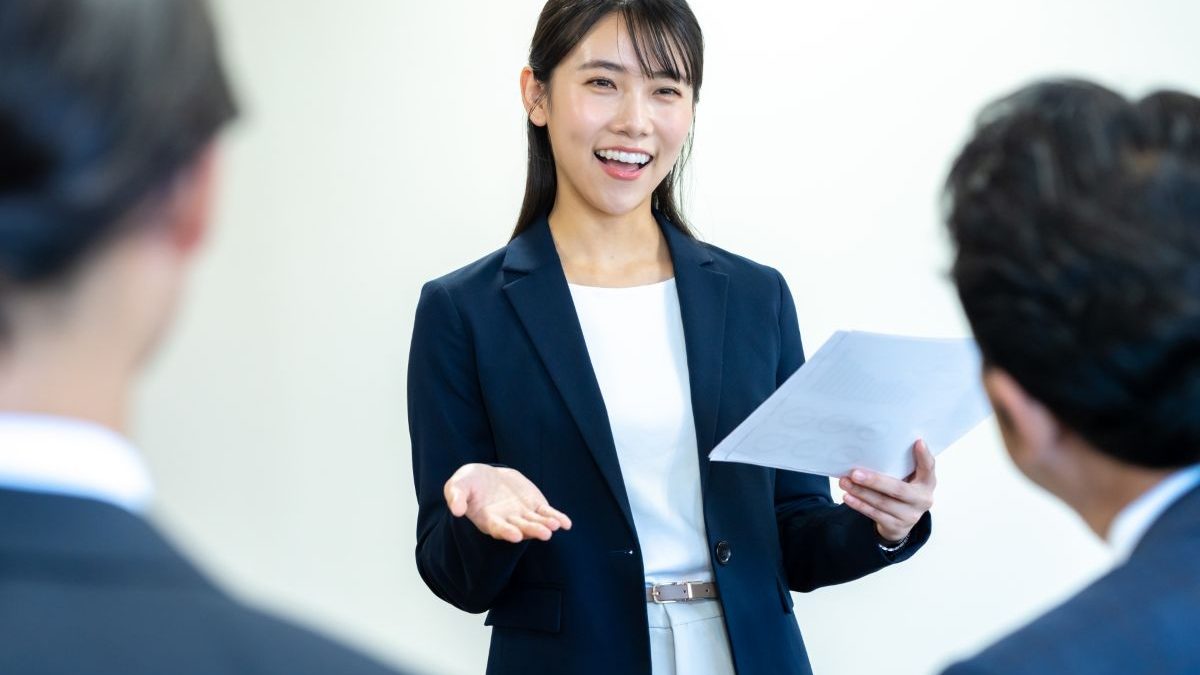 A young woman in a suit giving a presentation with a cheerful smile.