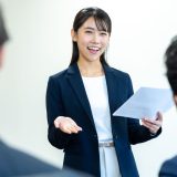 A young woman in a suit giving a presentation with a cheerful smile.