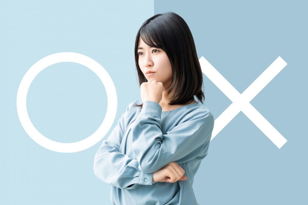 女性があごに手を当てて考えている画像。背景には〇とⅩが大きく表示されている。