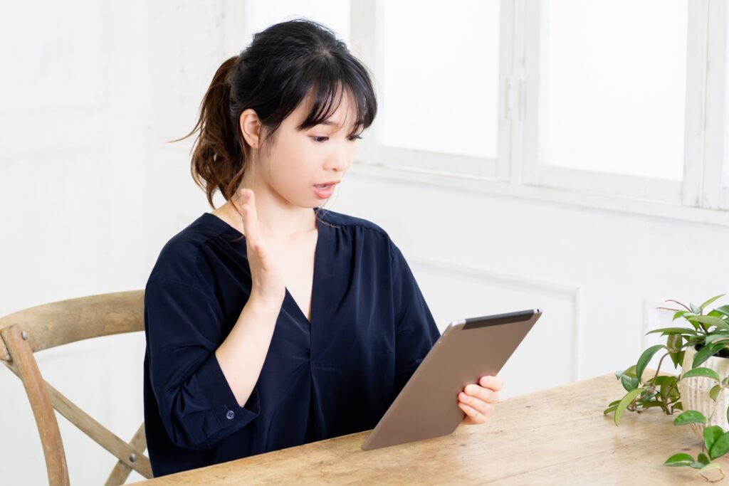 タブレットを見ながら表情豊かに話す女性。プレゼンの手本を視聴し、真似て練習している様子。