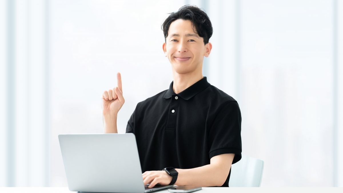 A confident male coach sitting in front of a laptop, raising his finger as he offers guidance. Represents trust and insight in the coaching process.