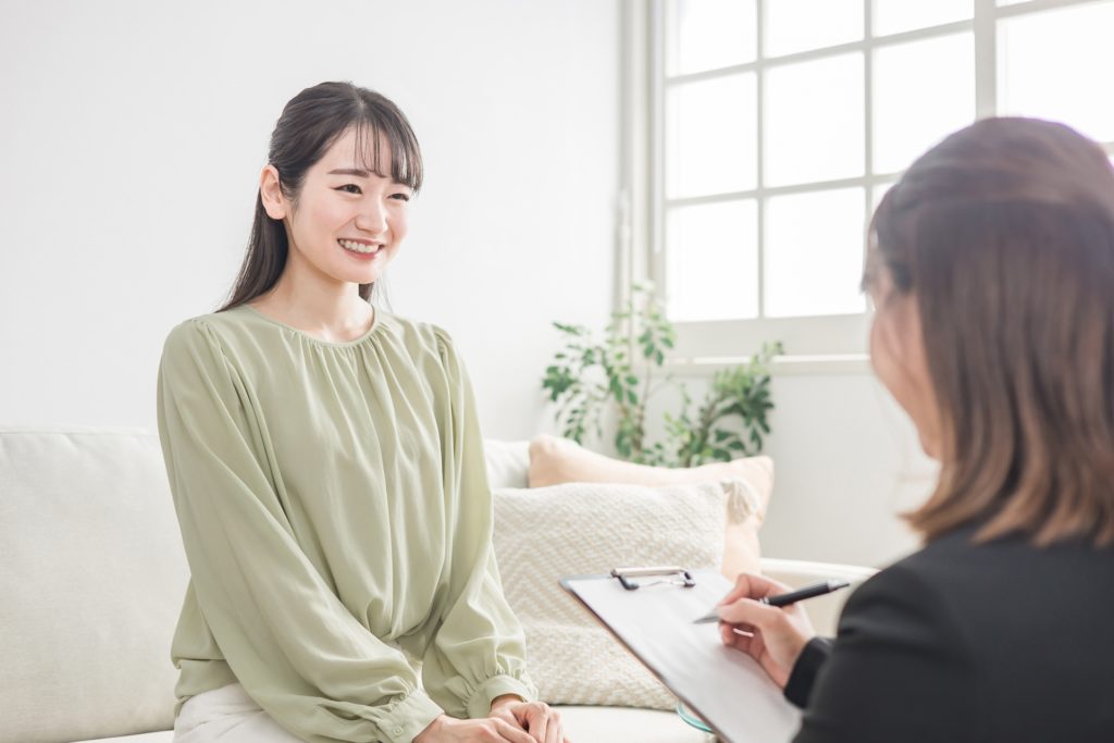 明るい部屋でカウンセラーと向き合い、穏やかに話す女性。安心感のあるカウンセリングの雰囲気を表現。
