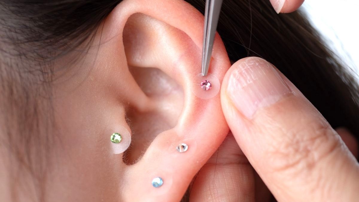 A close-up image of ear acupressure jewelry being gently applied, representing a self-care practice for beauty and health.