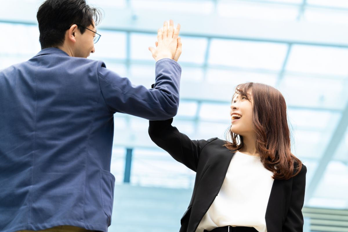 An image of a male and female businessperson smiling and sharing a high five in an office, celebrating success.