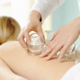 An image of a practitioner carefully placing glass cupping cups on a person’s back.