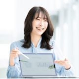 A smiling woman explaining a presentation using a laptop in a bright office. She appears confident and engaging.
